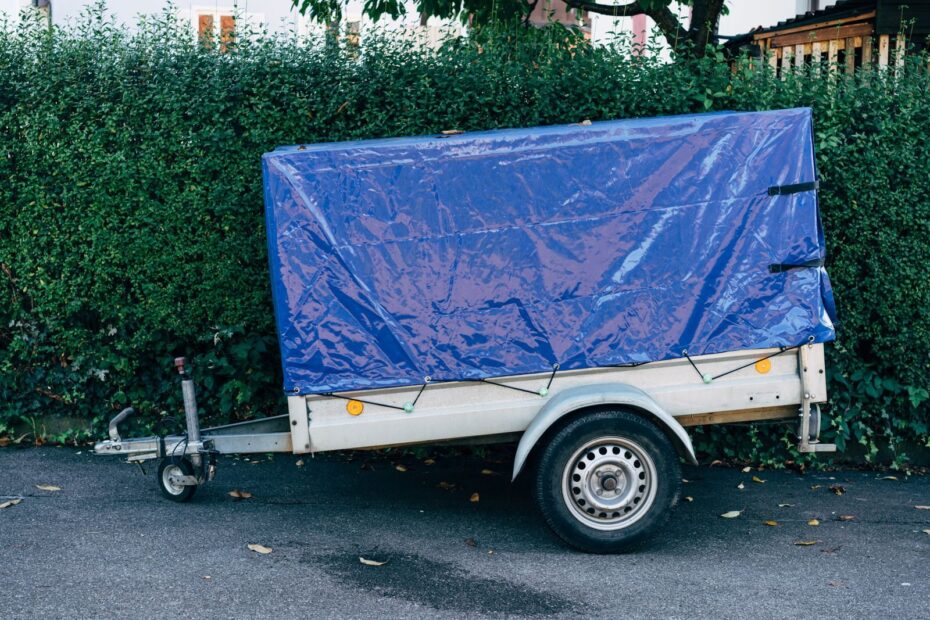 A blue tarpaulin-covered trailer parked on a roadside against a hedge, ideal for transport themes.