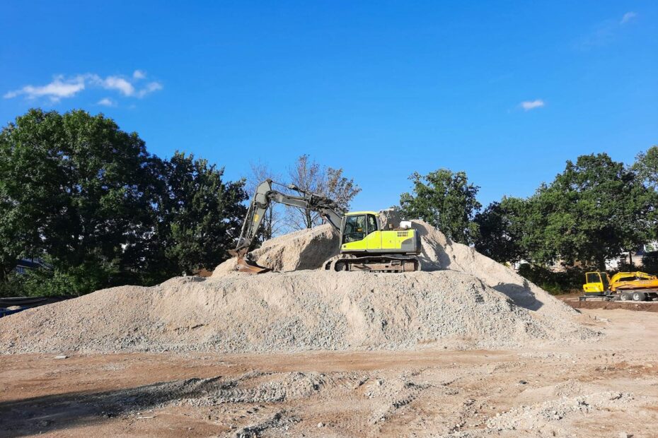 Excavator working on a gravel pile at an outdoor construction site with clear blue sky.